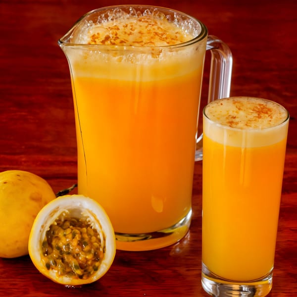 Pitcher and glass of frothy yellow passion fruit juice with whole and halved fruit.