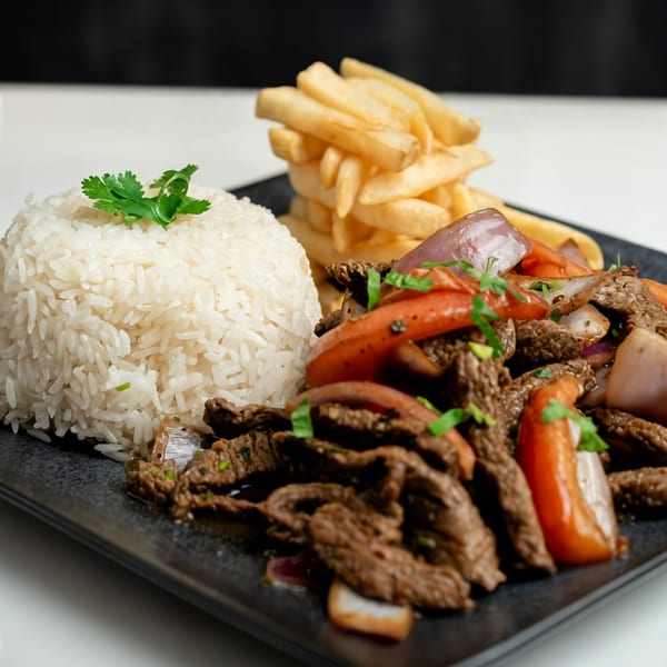 Peruvian Lomo Saltado with beef, red onions, tomatoes, rice, and french fries on a black plate.