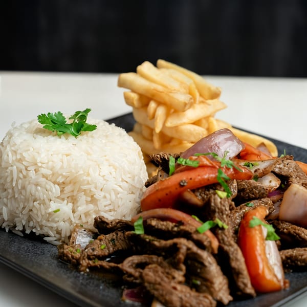 Peruvian Lomo Saltado with beef, red onions, tomatoes, rice, and french fries on a black plate.