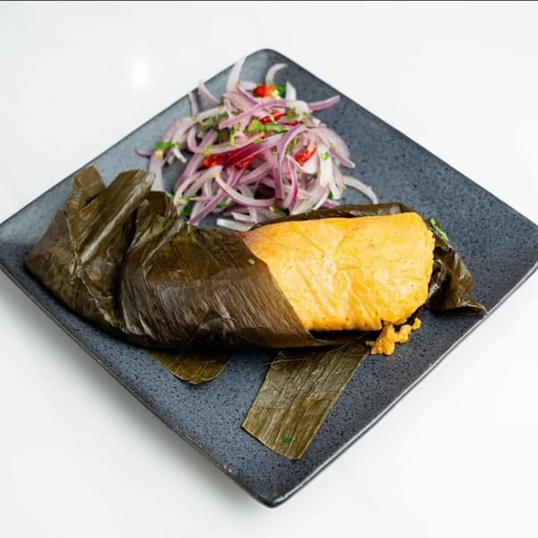 Peruvian tamal, a yellow corn masa dish wrapped in a banana leaf, served with red onion salsa.