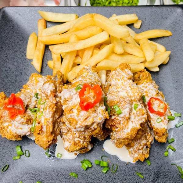 Crispy fried chicken pieces drizzled with white sauce, garnished with red peppers and green onions, served with fries.