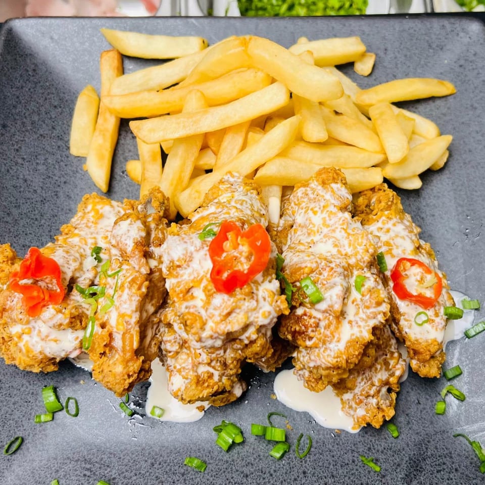 Crispy fried chicken pieces drizzled with white sauce, garnished with red peppers and green onions, served with fries.