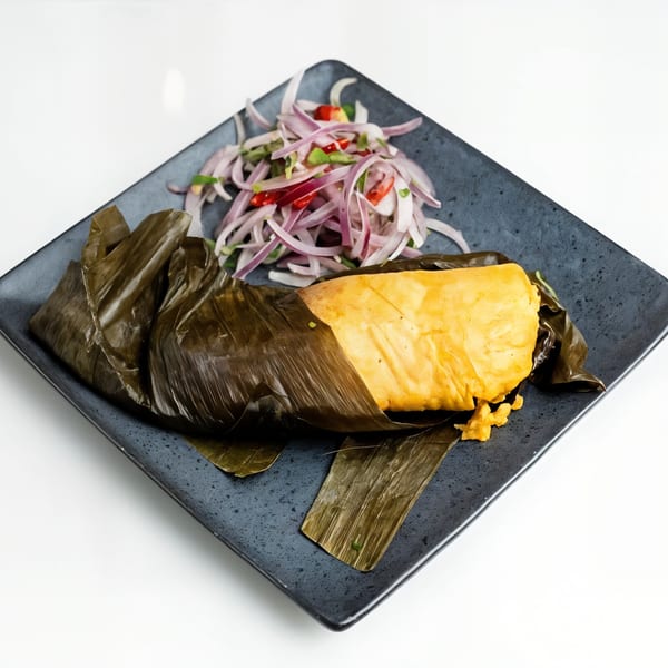 Peruvian tamale in a banana leaf with red onion and chili salsa on a dark plate.