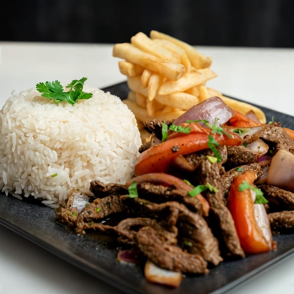 Peruvian Lomo Saltado with beef, red onions, tomatoes, rice, and french fries on a black plate.